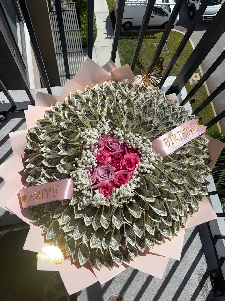 Money bouquet of folded dollar bills around pink and lavender roses, with a Happy Birthday sash and gold butterflies on pink wrapping
