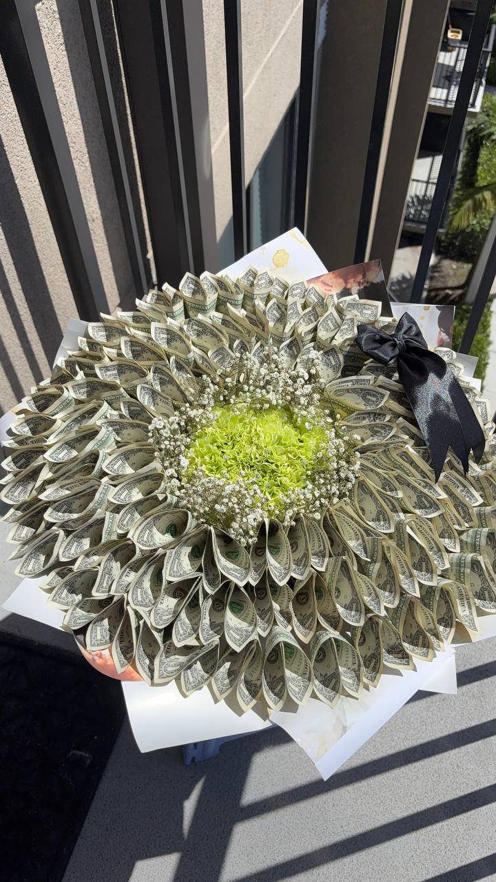 Money bouquet of folded dollar bills around a lime-green carnation center with baby's breath and a black bow