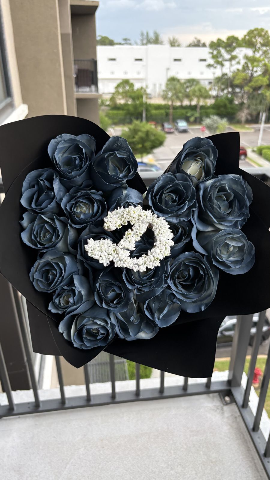 Dark blue roses in black wrapping with a baby's breath initial in the center, held on a balcony