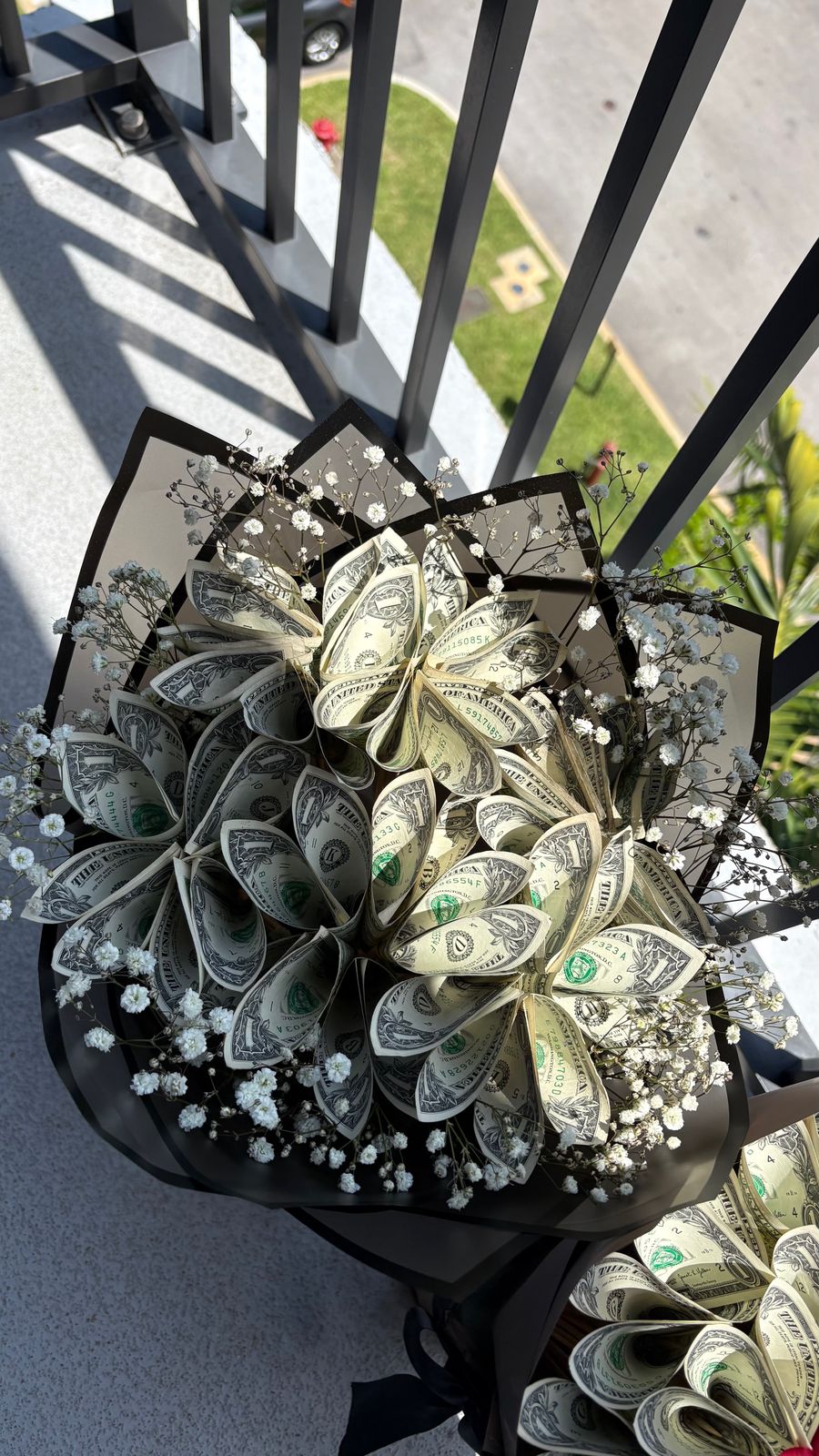 Large bouquet of folded dollar-bill flowers and baby's breath in black wrapping, held on a balcony
