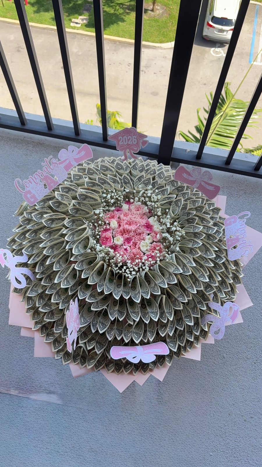 Tiered dollar-bill bouquet with a center of pink roses and baby's breath, decorated with pink bows and topper charms