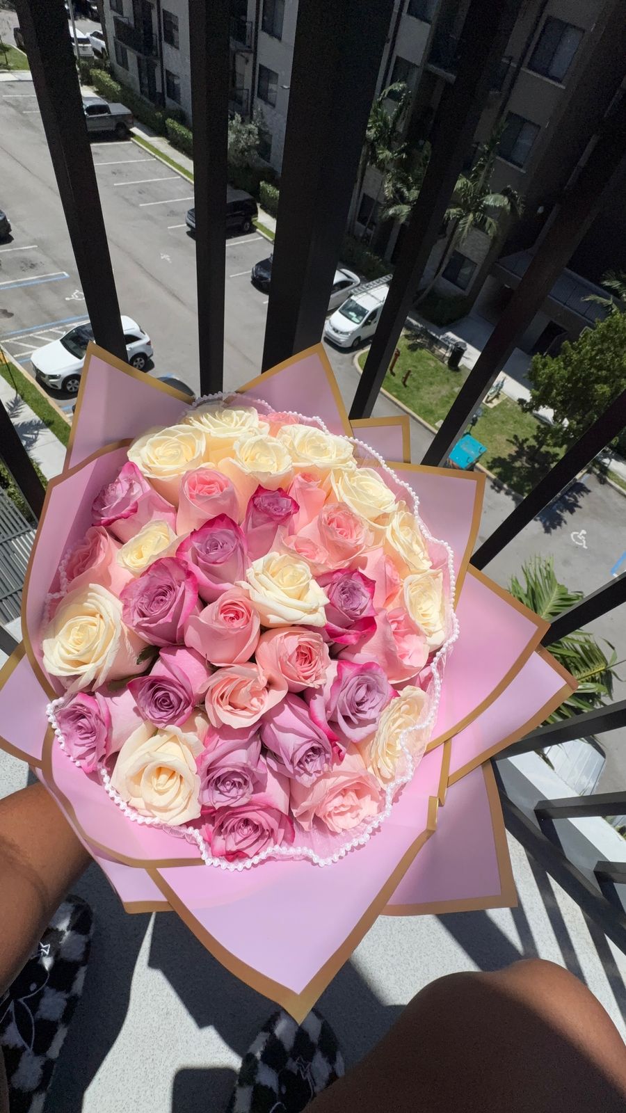 Pink, peach and cream roses in pink wrapping edged in gold and pearls, held over a balcony